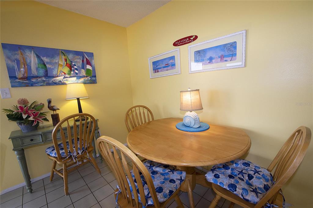 A dining area features a round wooden table, four chairs with patterned cushions, and yellow walls — 1571 S ATLANTIC AVENUE UNIT 312, NEW SMYRNA BEACH, FL