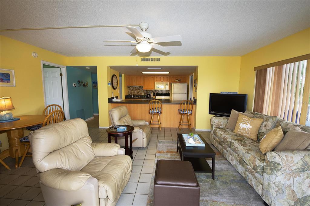 A living room with yellow walls, tile floors, a ceiling fan, and an open kitchen — 1571 S ATLANTIC AVENUE UNIT 312, NEW SMYRNA BEACH, FL