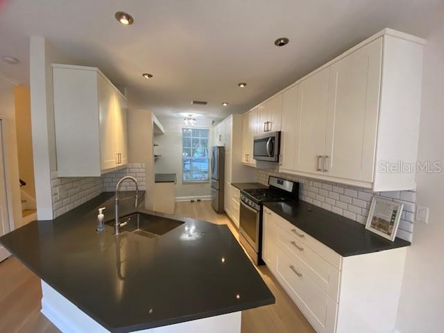 A kitchen features white cabinets, dark countertops, a stainless steel sink, and subway tile backsplash — 10034 TATE LANE, TAMPA, FL