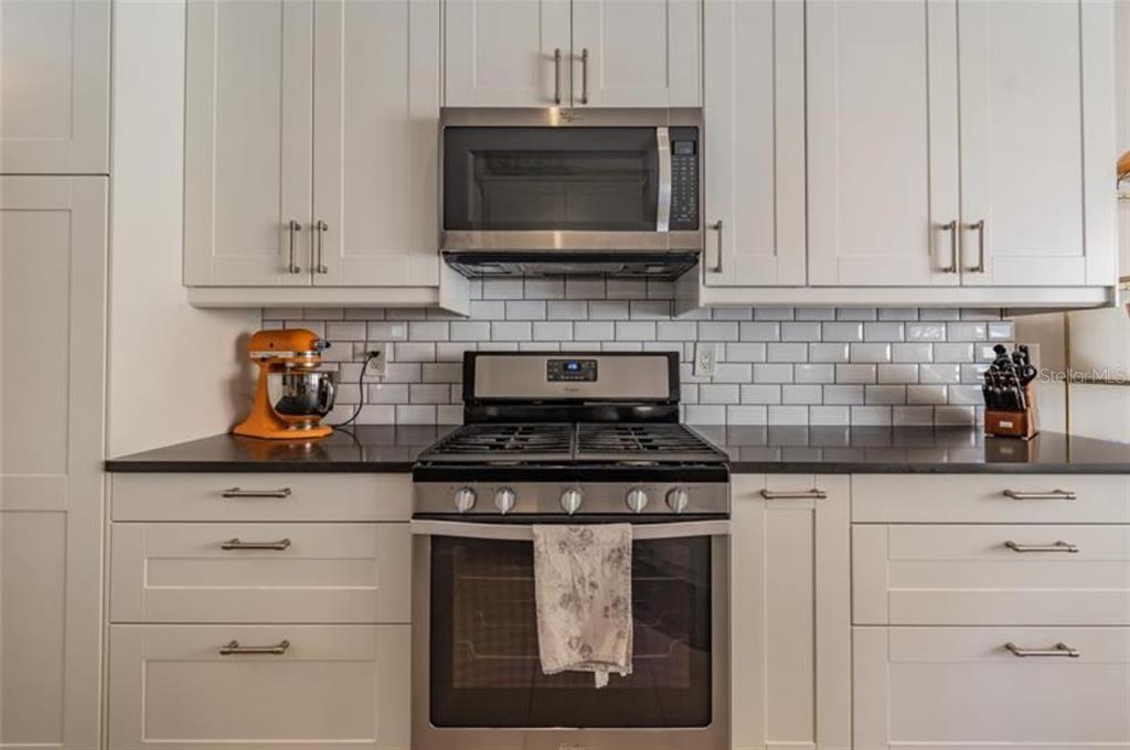 A kitchen features white cabinets, a stainless steel microwave and stove, and a subway tile backsplash — 10034 TATE LANE, TAMPA, FL
