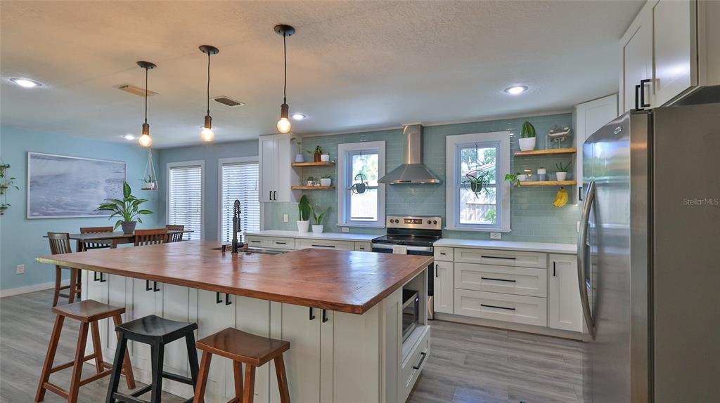 A kitchen features a large wooden island, white cabinetry, light blue tile backsplash, and stainless appliances — 2766 DATE PALM DRIVE, EDGEWATER, FL