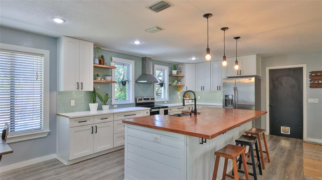 A kitchen features white cabinets, a wood-topped island, and light green subway tile backsplash — 2766 DATE PALM DRIVE, EDGEWATER, FL