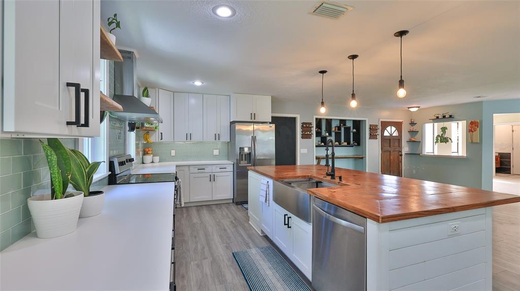 A kitchen features white cabinets, a wood-topped island with a farmhouse sink, and light flooring — 2766 DATE PALM DRIVE, EDGEWATER, FL