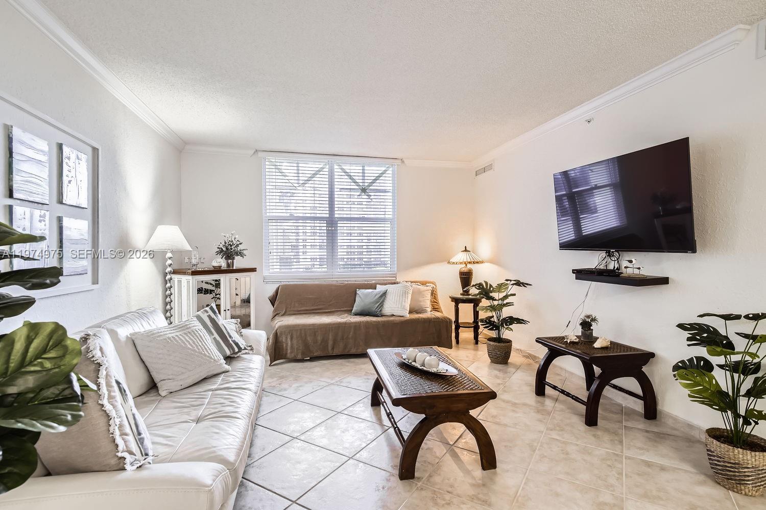 A living room features a white sofa, a brown daybed, a coffee table, and a wall-mounted television — 2501 S Ocean Dr, Hollywood FL 33019, HOLLYWOOD, FL