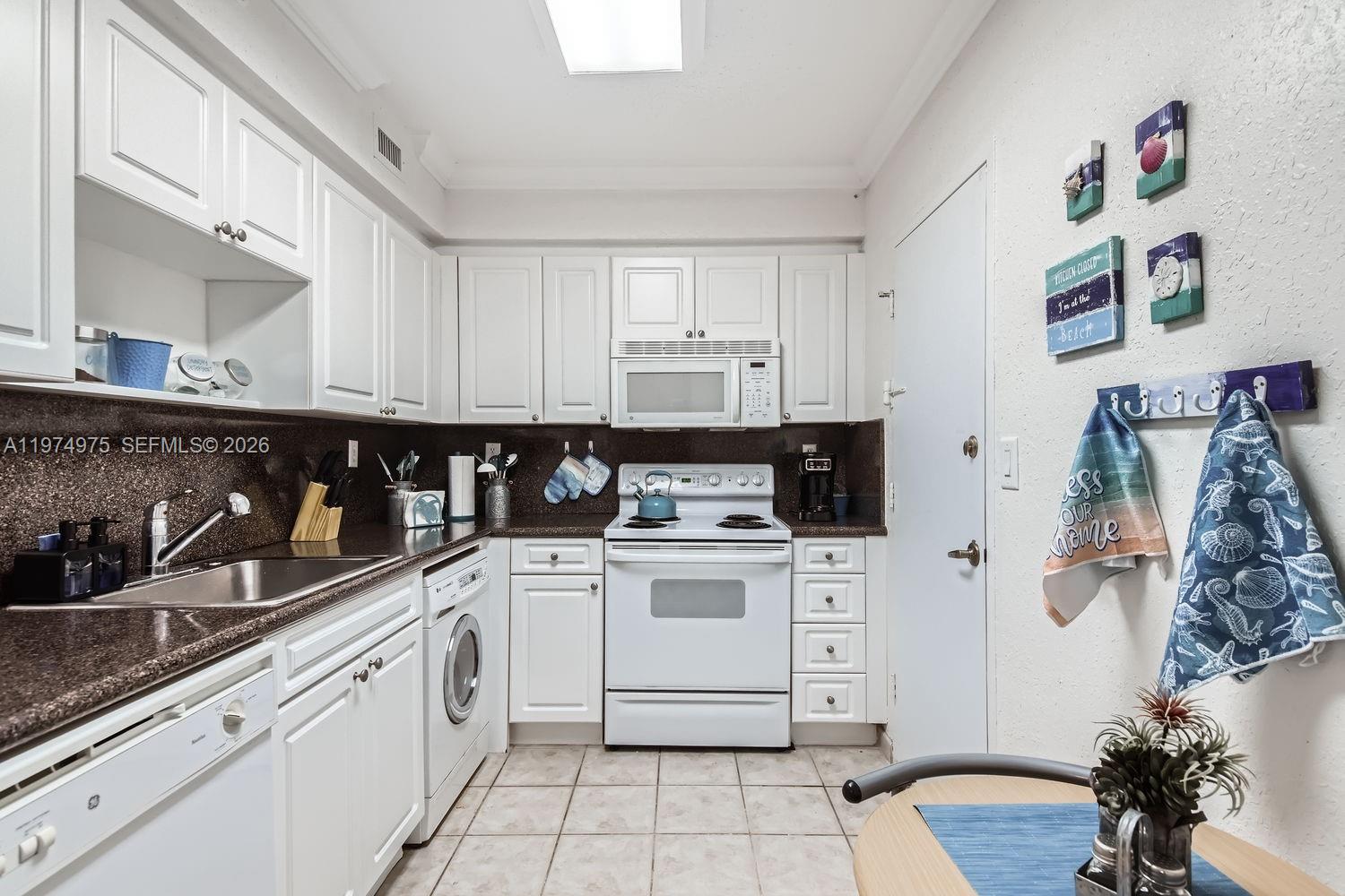 A white kitchen features dark countertops, stainless steel appliances, and a built-in laundry machine — 2501 S Ocean Dr, Hollywood FL 33019, HOLLYWOOD, FL