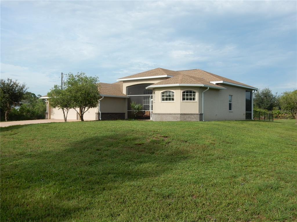 A single-story tan house with a screened-in porch and a large grassy front yard — 8430 ACORN BOULEVARD, PUNTA GORDA, FL
