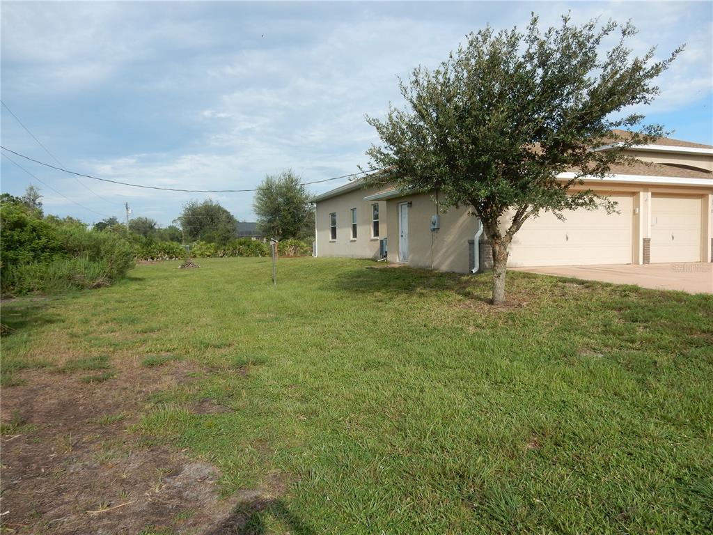 A side view of a tan house with a garage and a large grassy yard — 8430 ACORN BOULEVARD, PUNTA GORDA, FL