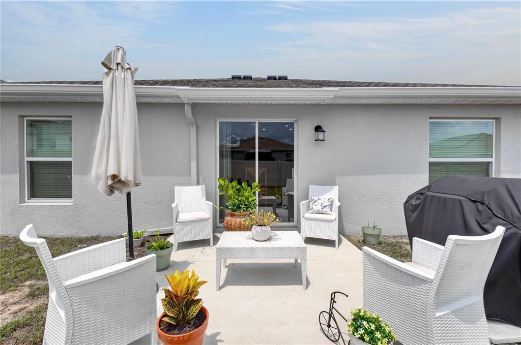 A concrete patio features white wicker chairs, a matching coffee table, and potted plants — 598 TANARO LANE, HAINES CITY, FL