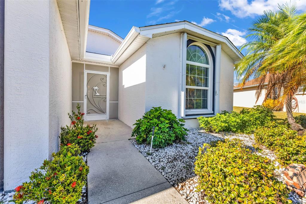 A concrete walkway leads to a white house with a decorative screen door and landscaping — 1713 PALACE COURT, PUNTA GORDA, FL