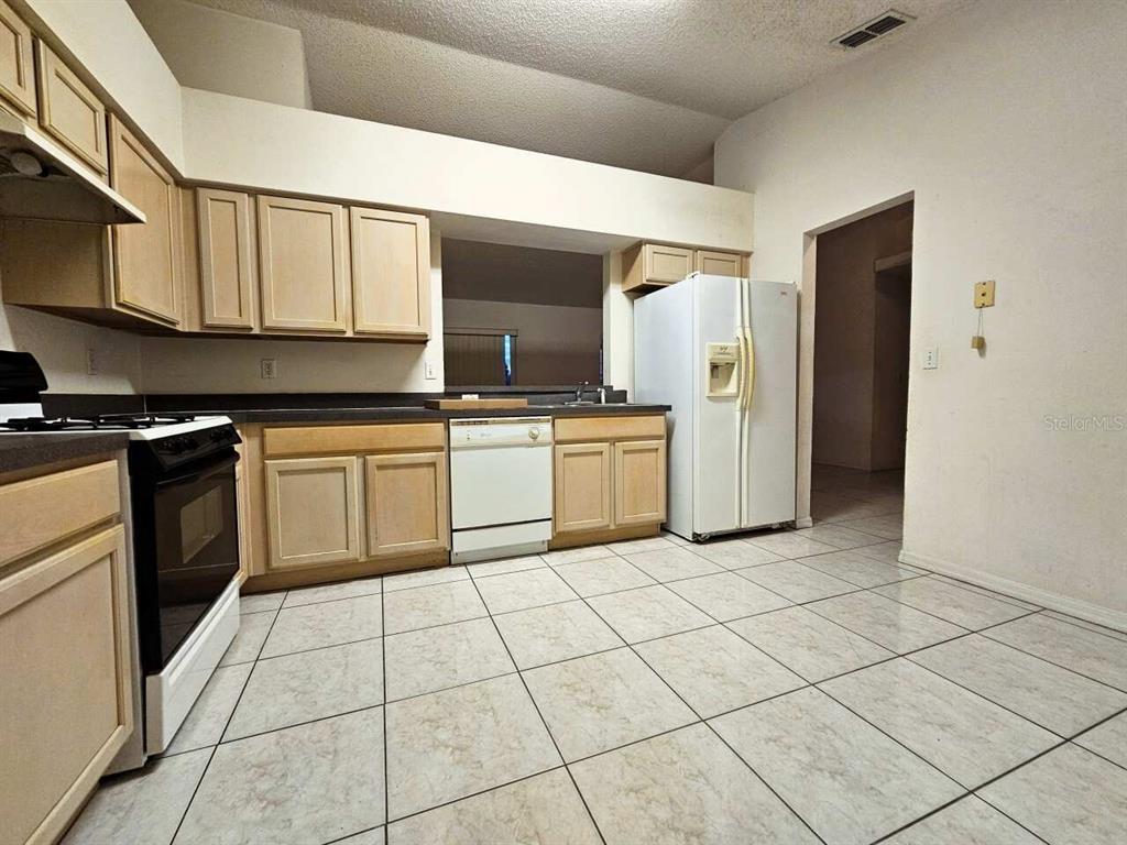 A kitchen with light wood cabinets, white appliances, and light-colored tiled flooring — 13345 PINYON DRIVE, CLERMONT, FL