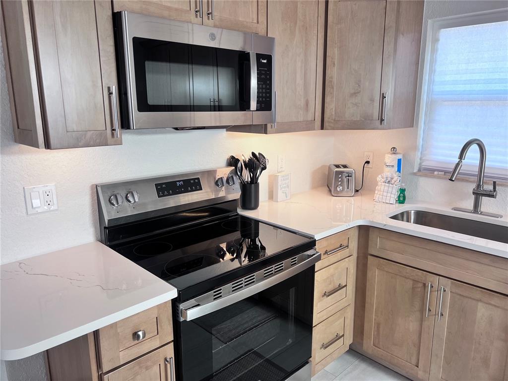 A kitchen features light wood cabinets, stainless steel appliances, and white quartz countertops — 6154 MIDNIGHT PASS ROAD UNIT B06, SARASOTA, FL