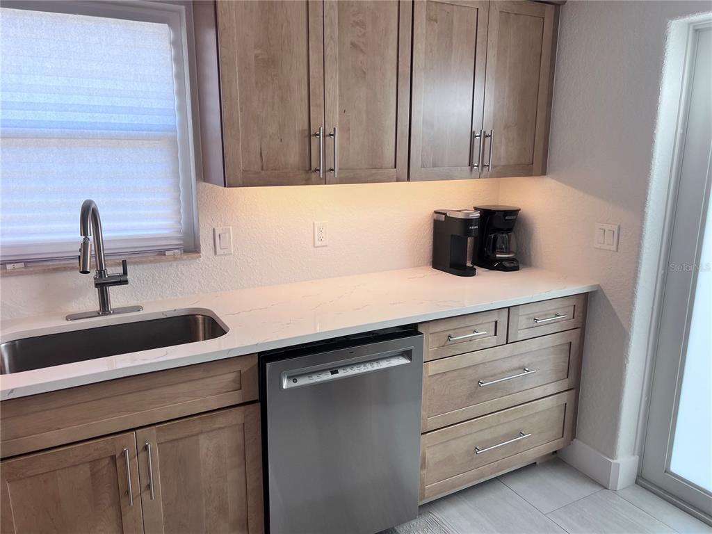 A kitchen features light wood cabinets, white quartz countertops, stainless steel appliances, and under-cabinet lighting — 6154 MIDNIGHT PASS ROAD UNIT B06, SARASOTA, FL