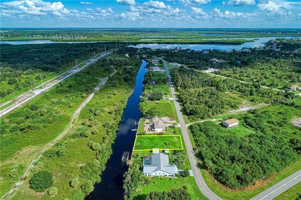 An aerial view shows a vacant rectangular lot outlined in yellow next to a canal — 27202 SAN MARCO DRIVE, PUNTA GORDA, FL