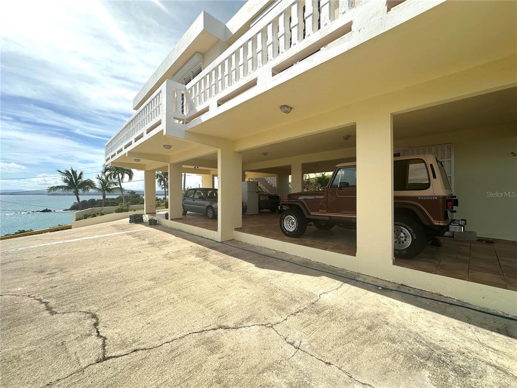 A concrete driveway leads to a covered parking area beneath a two-story coastal home — 38 FLOR MARINA MAR CARIBE, NAGUABO, PR