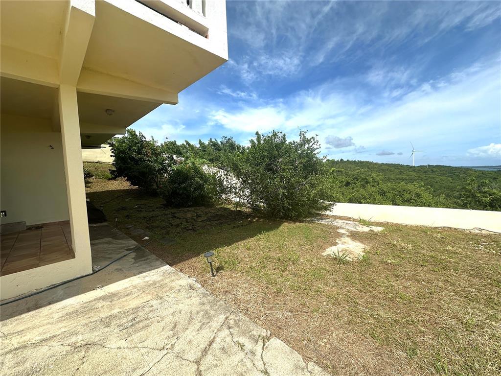 A concrete patio overlooks a grassy yard with bushes and a distant wind turbine — 38 FLOR MARINA MAR CARIBE, NAGUABO, PR