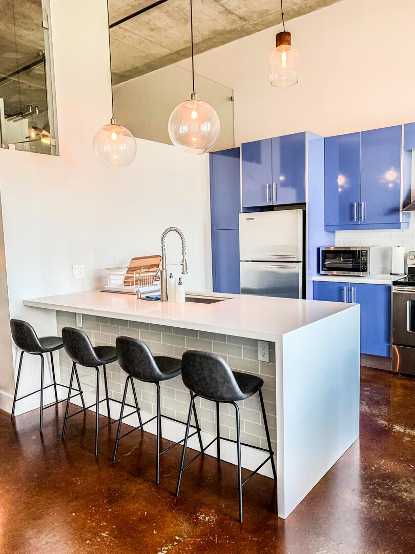 A modern kitchen features a white island with bar stools, blue cabinets, and concrete ceilings — 185 NE 4th Avenue # 204, Delray Beach FL 33483, DELRAY BEACH, FL