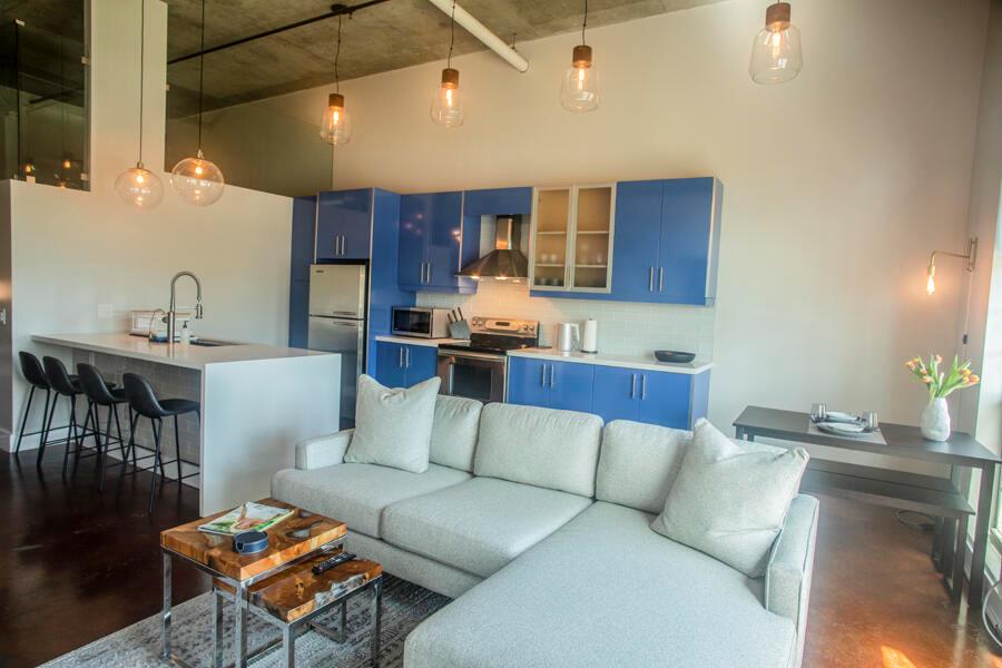An open-concept living room and kitchen featuring blue cabinets, a sectional sofa, and pendant lighting — 185 NE 4th Avenue # 204, Delray Beach FL 33483, DELRAY BEACH, FL