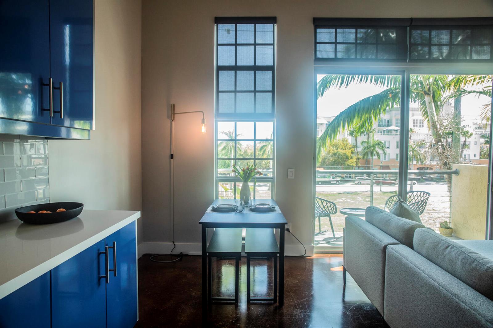 A kitchen and dining area with blue cabinets, a small table, and a balcony view — 185 NE 4th Avenue # 204, Delray Beach FL 33483, DELRAY BEACH, FL