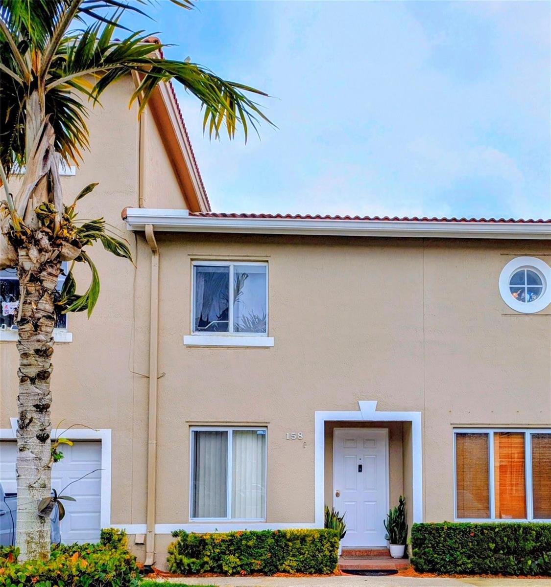 A two-story tan townhouse exterior features a white front door, a palm tree, and landscaping — 158 Riviera Circle # 3, Weston FL 33326, WESTON, FL