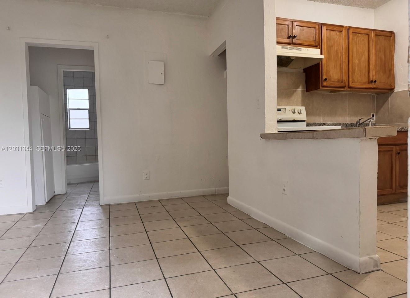 A tiled room features a kitchen pass-through window and an adjacent doorway leading to a bathroom — 1601 NW 62nd St # 26, Miami FL 33147, MIAMI, FL