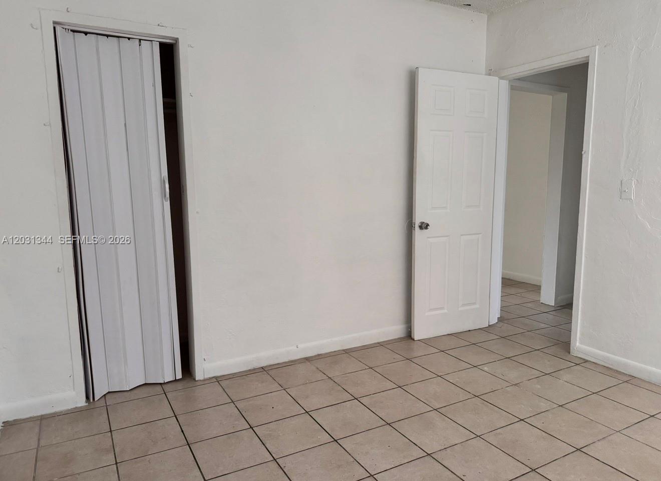 A room with white walls, tiled floors, a folding closet door, and an open doorway — 1601 NW 62nd St # 26, Miami FL 33147, MIAMI, FL