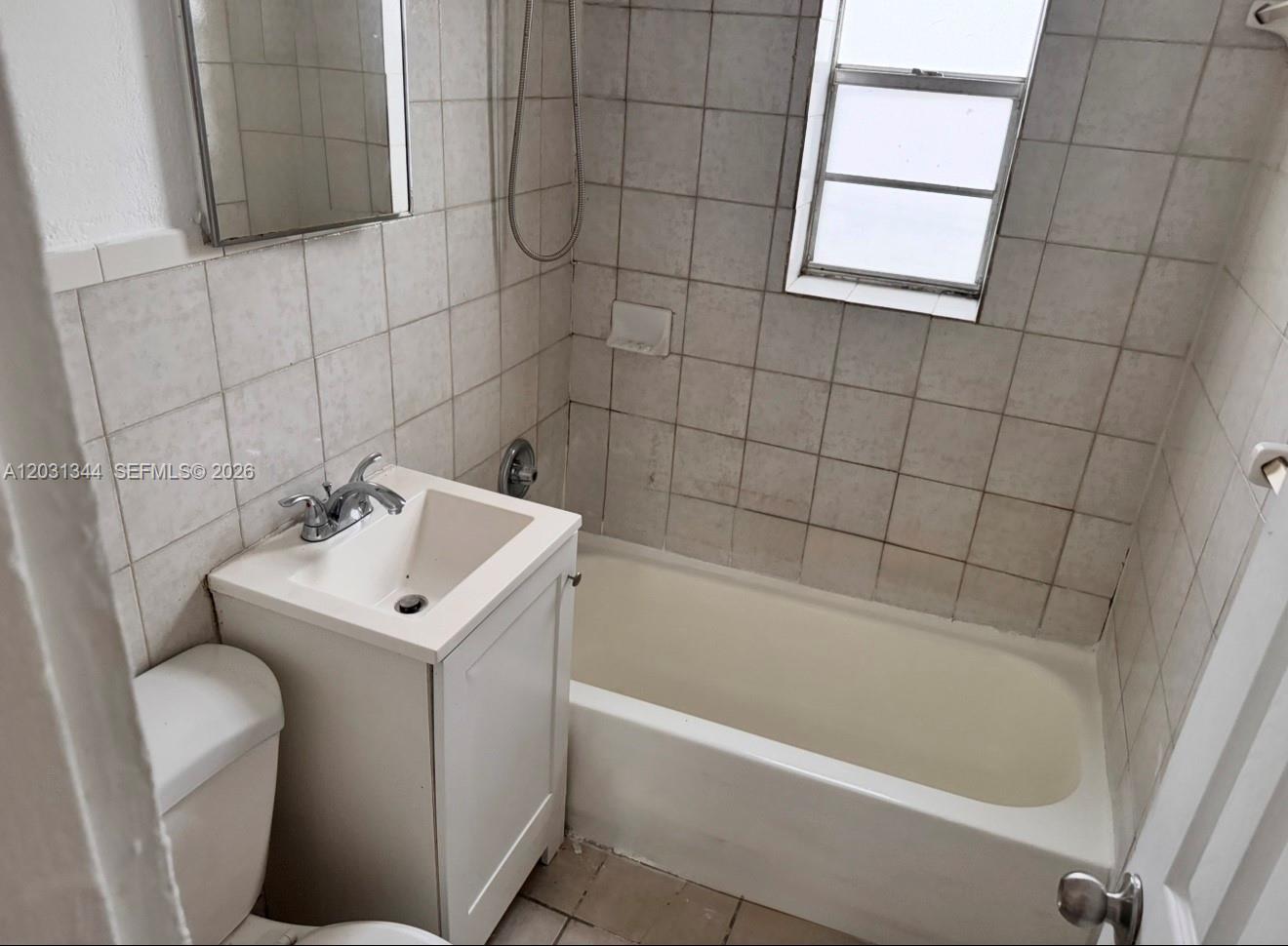 A small bathroom features a white vanity, a toilet, and a tiled tub-shower combination — 1601 NW 62nd St # 26, Miami FL 33147, MIAMI, FL