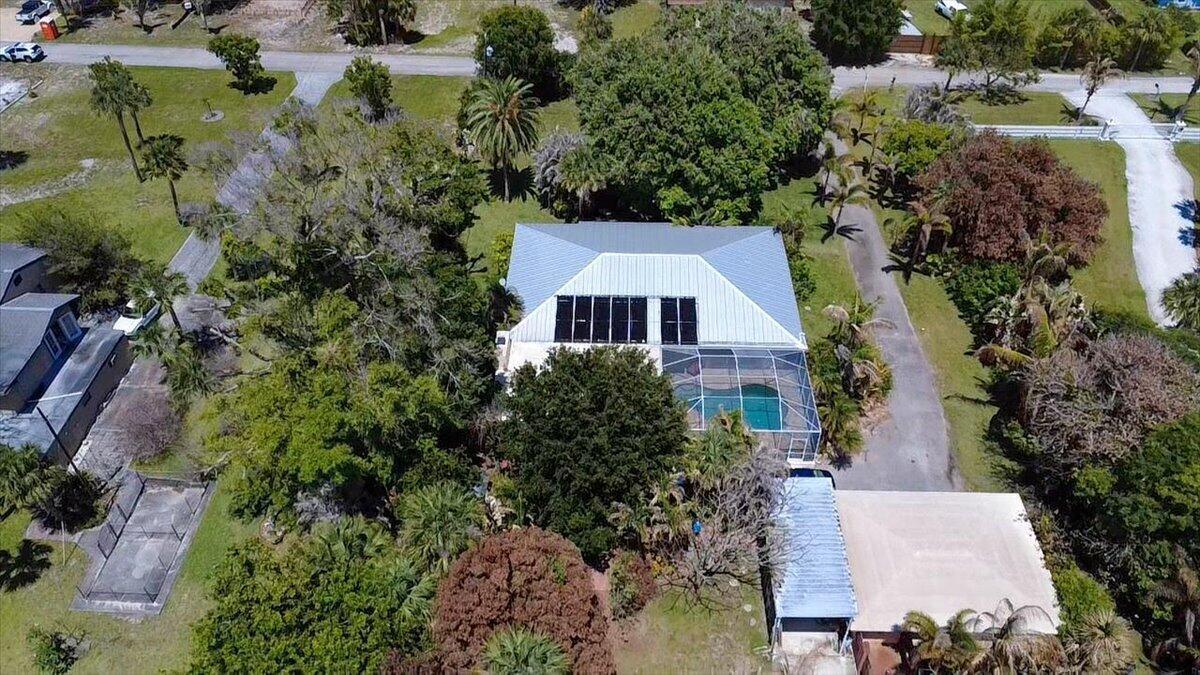An aerial view shows a house with solar panels, a screened pool, and a detached carport — 105 Sheridan Lane, Jensen Beach FL 34957, JENSEN BEACH, FL
