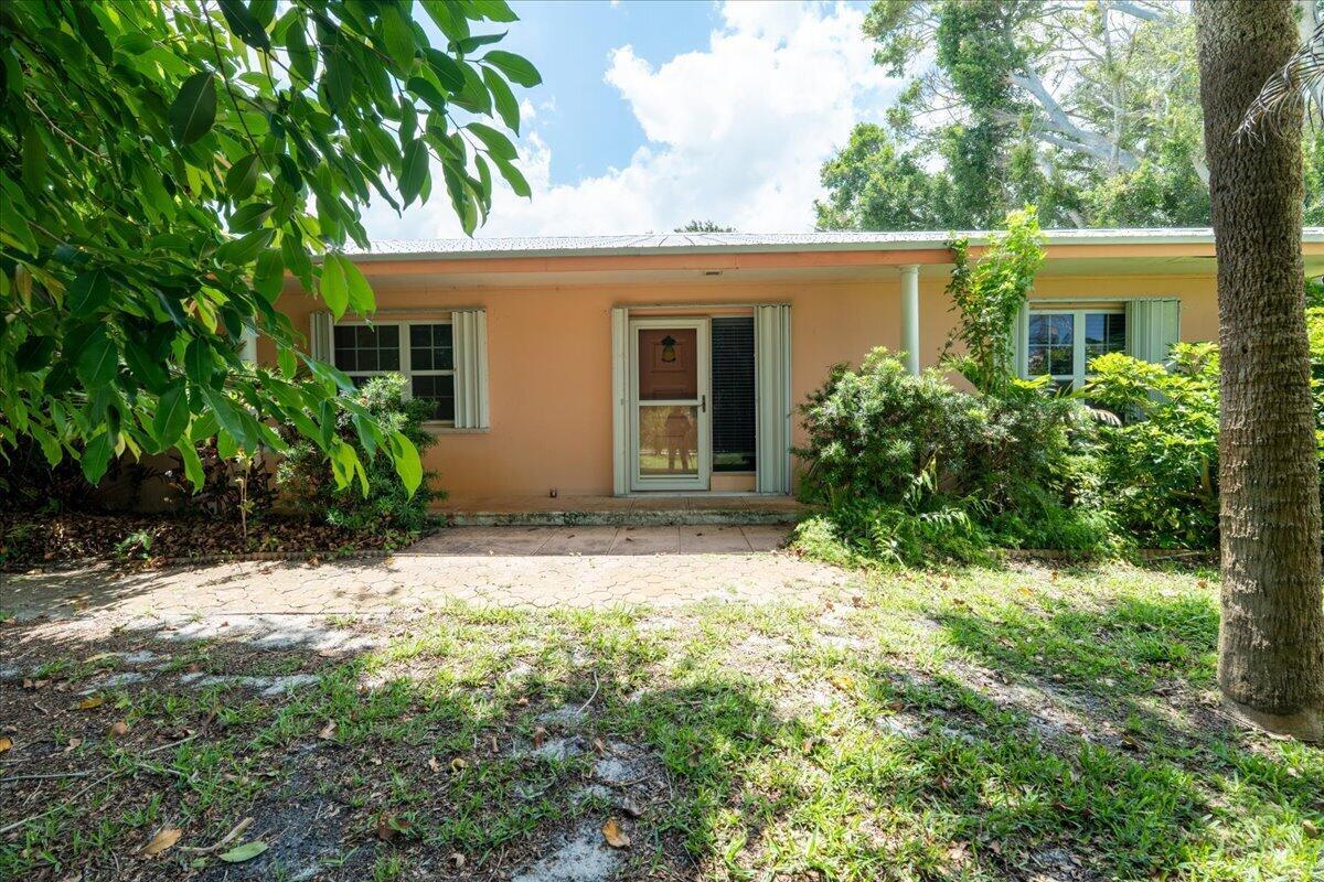 A peach-colored single-story house features a central glass door and a paved patio area — 105 Sheridan Lane, Jensen Beach FL 34957, JENSEN BEACH, FL