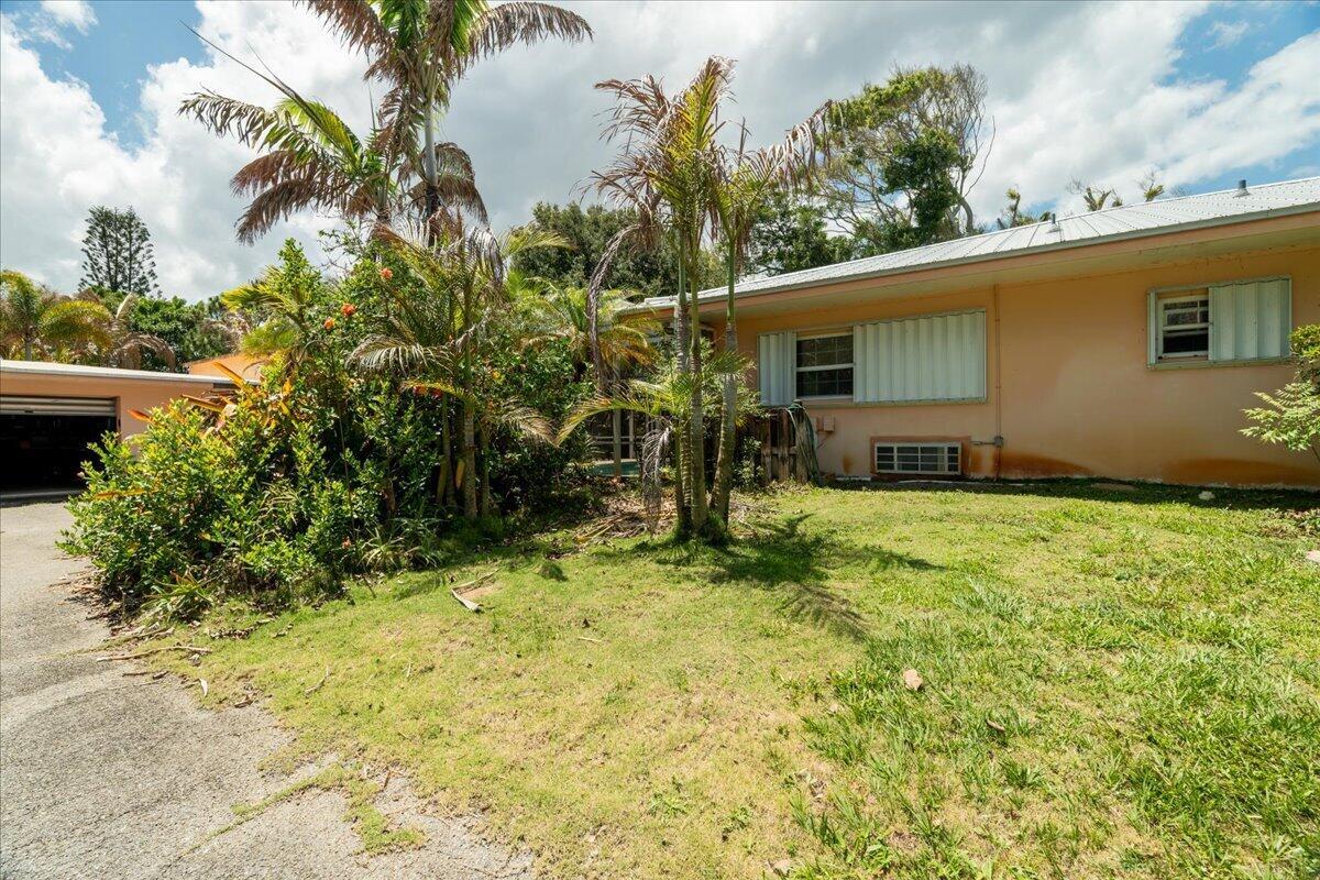 A single-story peach-colored house with a metal roof, palm trees, and a concrete driveway — 105 Sheridan Lane, Jensen Beach FL 34957, JENSEN BEACH, FL