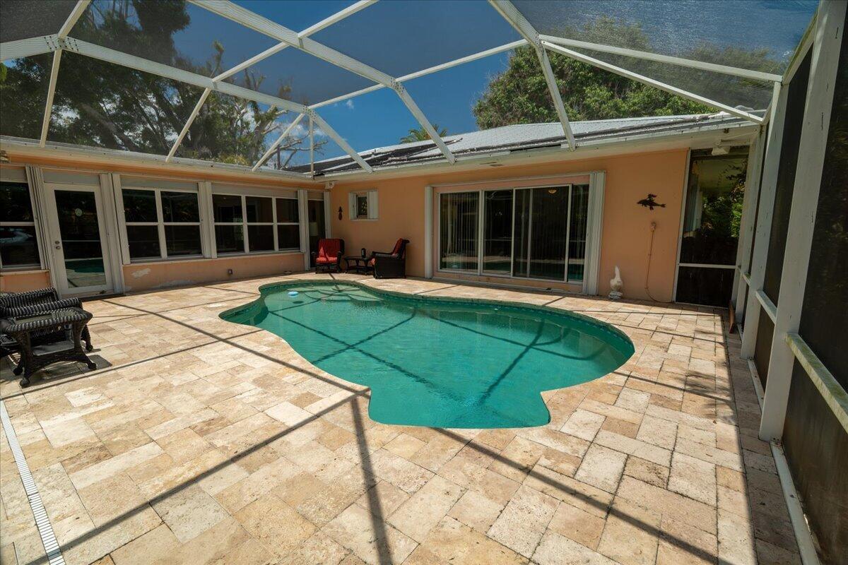 A screened-in patio features a kidney-shaped swimming pool surrounded by light-colored stone pavers — 105 Sheridan Lane, Jensen Beach FL 34957, JENSEN BEACH, FL