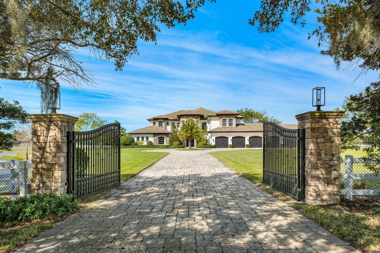 A paved driveway leads through stone pillars and iron gates toward a large suburban mansion — 10527 El Paraiso Place, Delray Beach FL 33446, DELRAY BEACH, FL