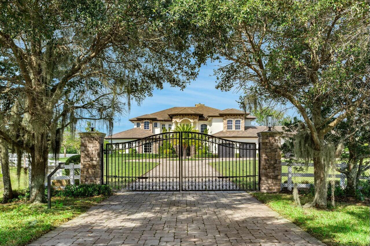 A large two-story house with a stone facade sits behind a black metal gated entrance — 10527 El Paraiso Place, Delray Beach FL 33446, DELRAY BEACH, FL