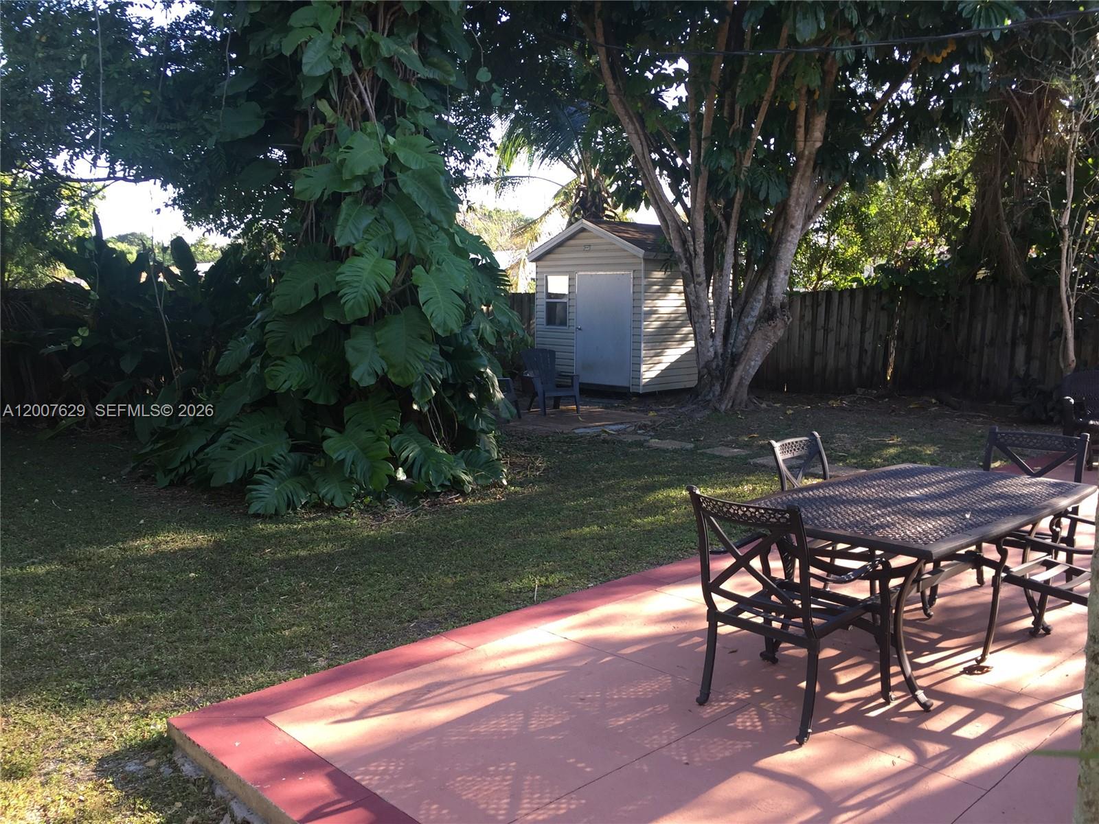 A patio with a metal dining set overlooks a backyard featuring a shed and trees — 5886 SW 42 St, Miami FL 33155, MIAMI, FL