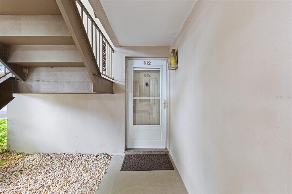 A white front door with a storm door is located beneath an outdoor staircase — 5265 E BAY DRIVE UNIT 612, CLEARWATER, FL