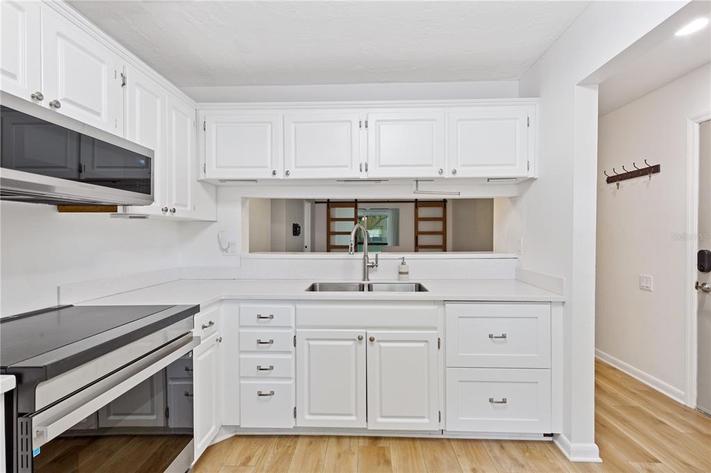 A white kitchen features a stainless steel oven, sink, and cabinets with light wood flooring — 5265 E BAY DRIVE UNIT 612, CLEARWATER, FL