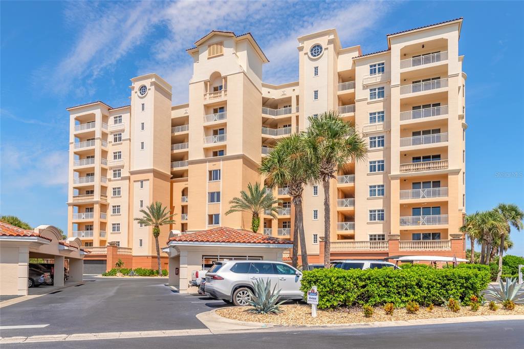 A multi-story tan apartment building with balconies and a parking area in the foreground — 263 MINORCA BEACH WAY UNIT 304, NEW SMYRNA BEACH, FL