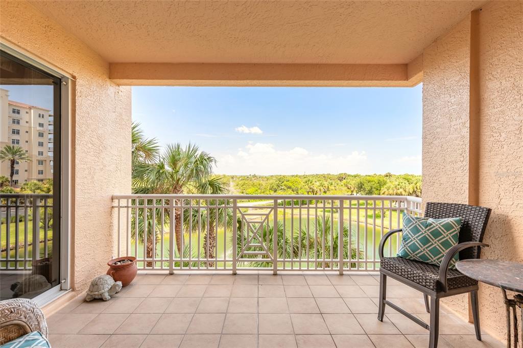 A tiled balcony features a metal railing, a wicker chair with a pillow, and outdoor views — 263 MINORCA BEACH WAY UNIT 304, NEW SMYRNA BEACH, FL