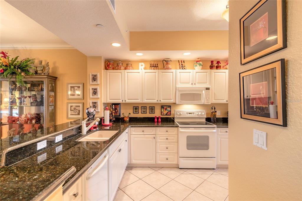 A kitchen features white cabinets, dark granite countertops, and a white stove — 263 MINORCA BEACH WAY UNIT 304, NEW SMYRNA BEACH, FL