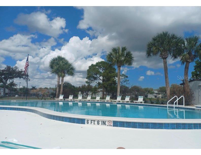 A swimming pool with lounge chairs and palm trees under a blue sky with clouds — 2250 CANDLEWOOD LANE E, NEW SMYRNA BEACH, FL
