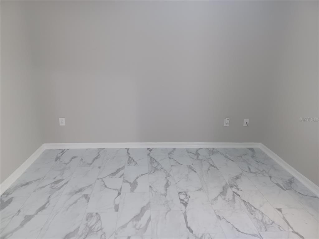 An empty room features light gray walls, white baseboards, and white marble-patterned tile flooring — 2250 CANDLEWOOD LANE E, NEW SMYRNA BEACH, FL