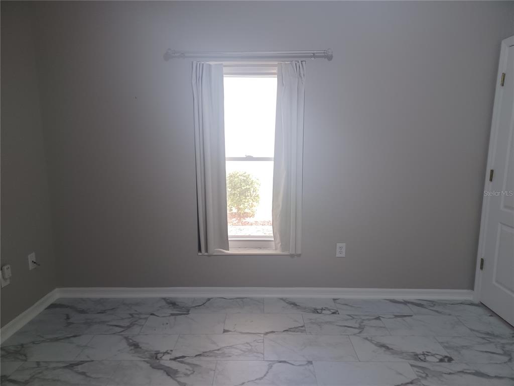 A room with gray walls, white baseboards, a single window with curtains, and marble-patterned tile flooring — 2250 CANDLEWOOD LANE E, NEW SMYRNA BEACH, FL