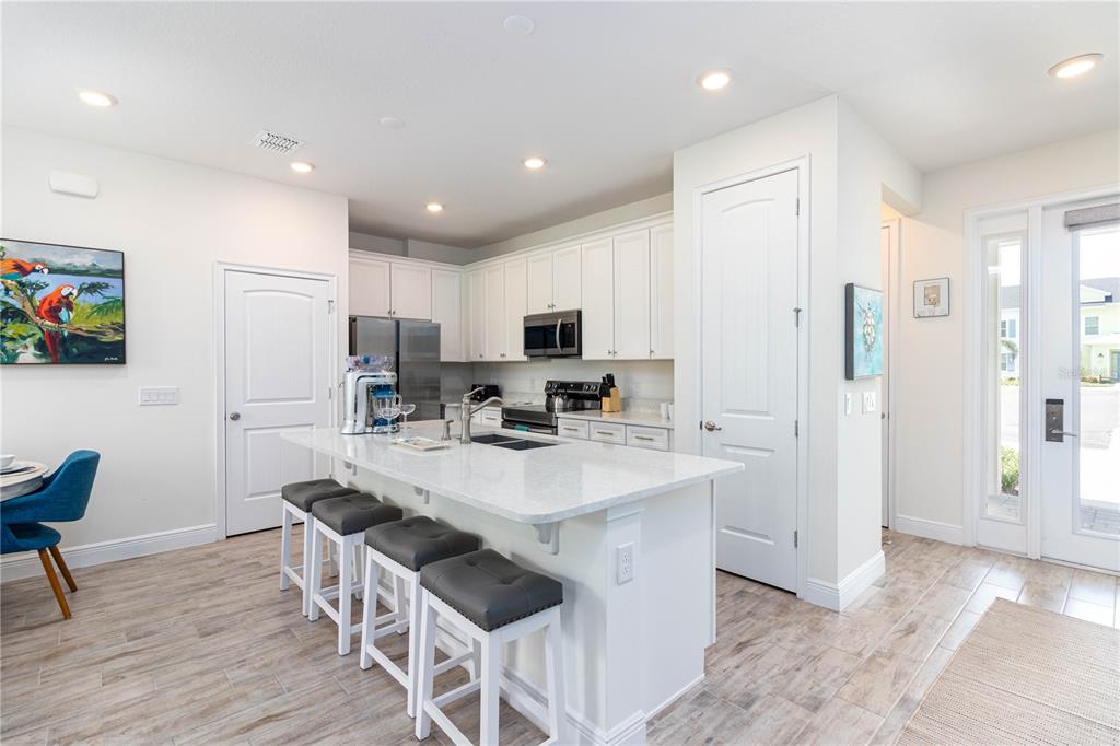 A modern kitchen features white cabinets, a quartz-topped island with stools, and light wood-look flooring — 2960 ON THE ROCKS POINT, KISSIMMEE, FL