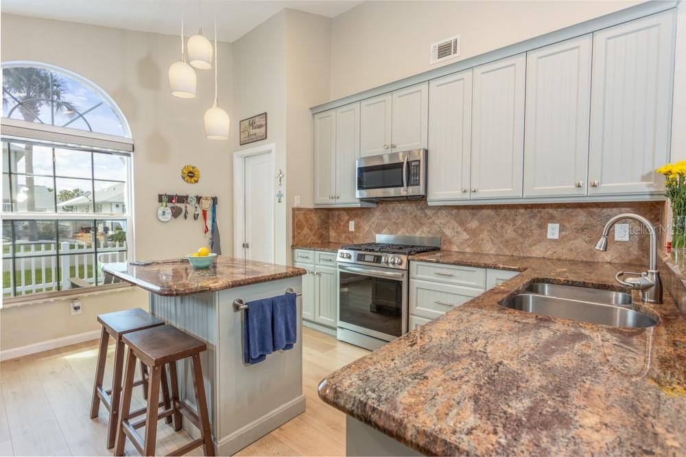 A kitchen with light blue cabinets, granite countertops, a center island, and a large window — 33 BEDFORD DRIVE, PALM COAST, FL