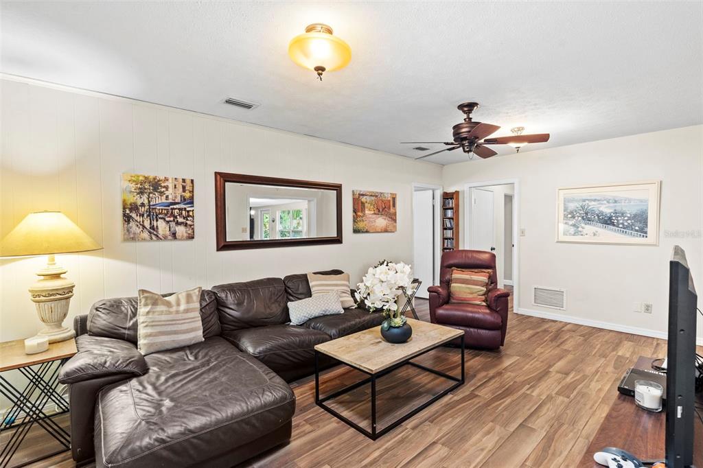 A hallway with wood-look flooring leads to a kitchen, with a piano room to the right — 4405 W MELROSE AVENUE, TAMPA, FL