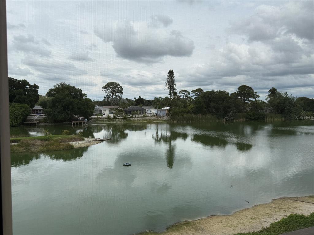 A view of a lake and residential houses from behind a screened-in porch — 5555 ASHTON LAKE DRIVE UNIT 5555, SARASOTA, FL