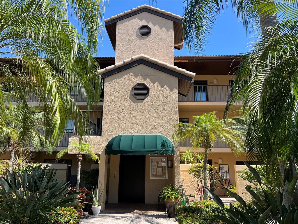 The exterior of a multi-story stucco apartment building features a central tower and green awning — 5555 ASHTON LAKE DRIVE UNIT 5555, SARASOTA, FL