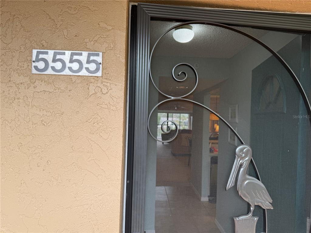 A silver pelican-shaped metal screen door is mounted on a tan stucco exterior wall — 5555 ASHTON LAKE DRIVE UNIT 5555, SARASOTA, FL