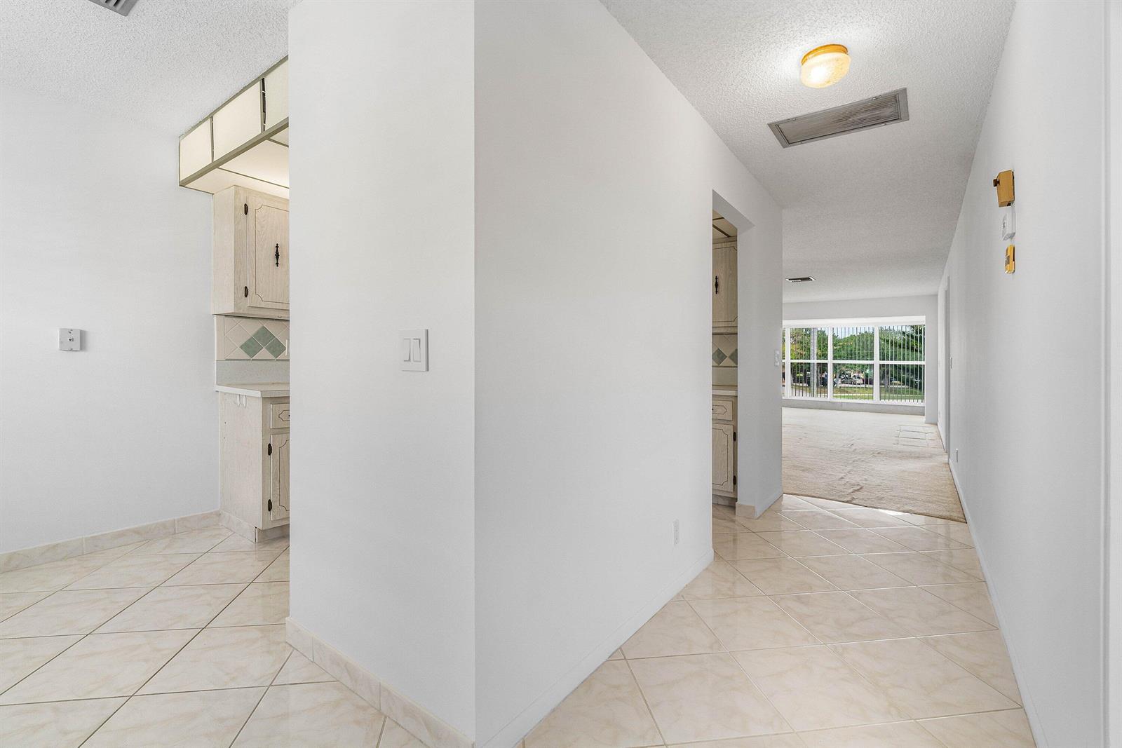 A tiled hallway leads to a carpeted living area with large windows and white cabinets — 2835 SW 13th Street # 202, Delray Beach FL 33445, DELRAY BEACH, FL