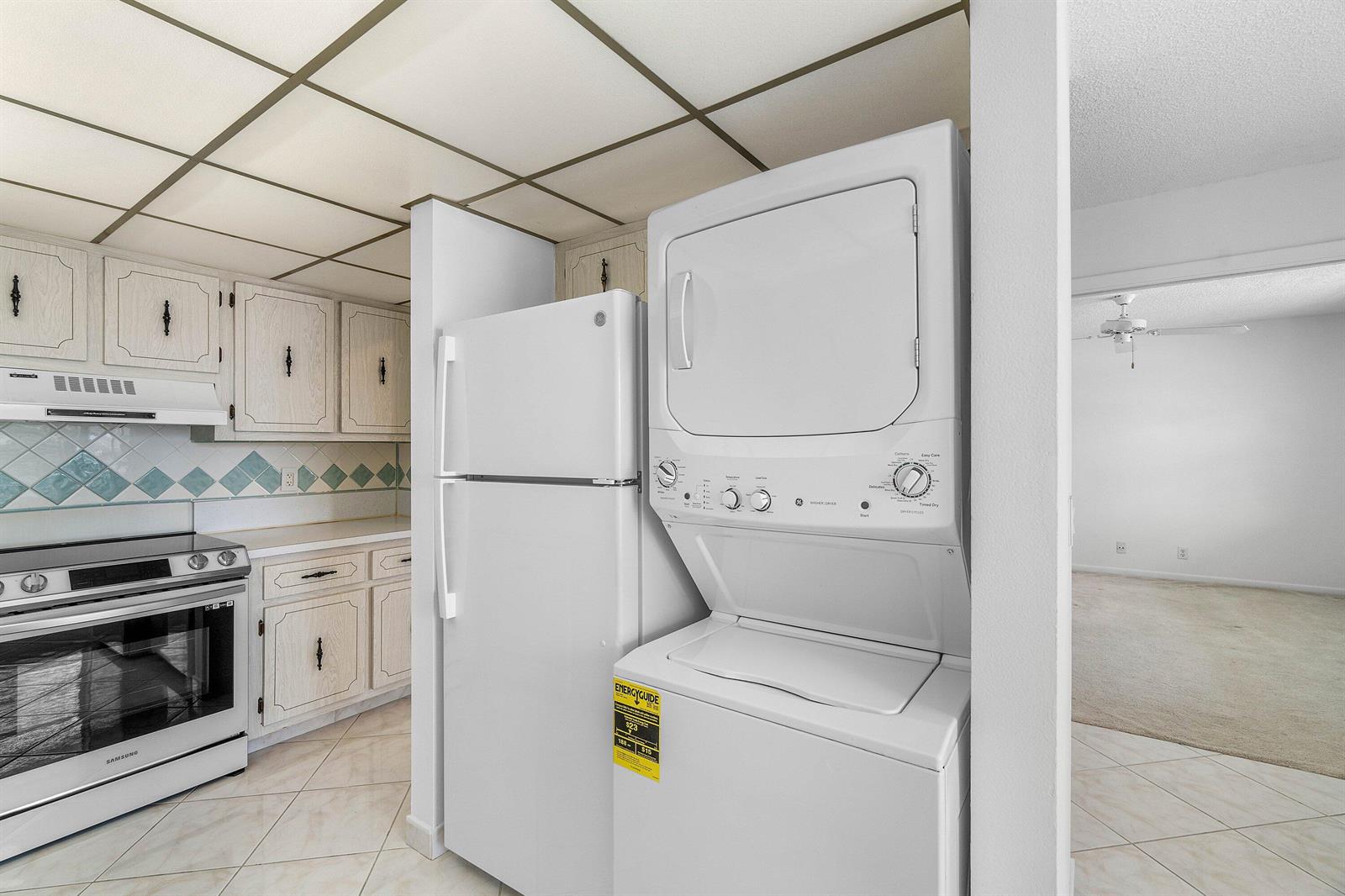 A kitchen features white cabinetry, a stacked washer-dryer unit, and a white refrigerator — 2835 SW 13th Street # 202, Delray Beach FL 33445, DELRAY BEACH, FL