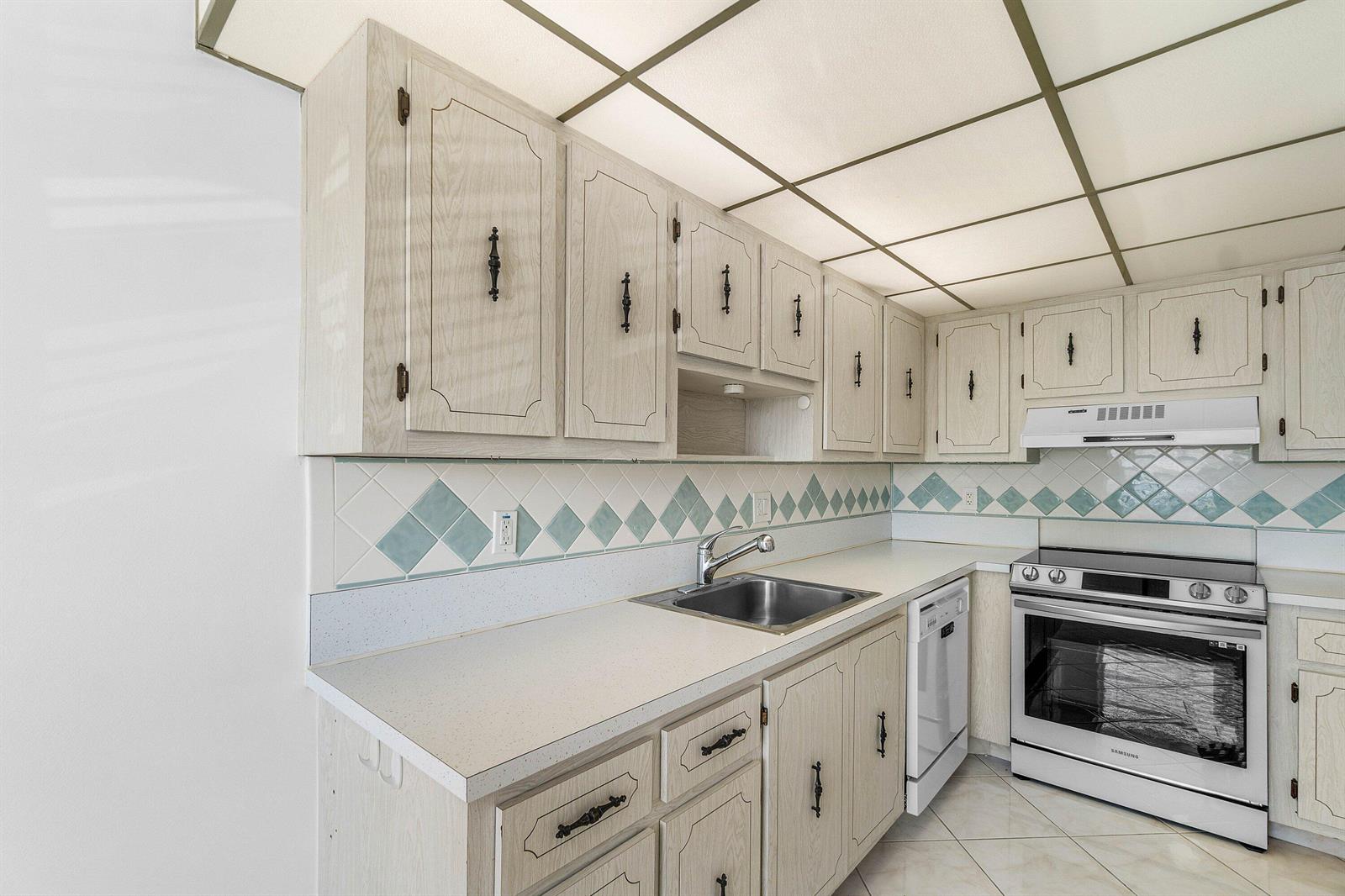 A kitchen features light wood cabinets, a tiled backsplash, and white appliances — 2835 SW 13th Street # 202, Delray Beach FL 33445, DELRAY BEACH, FL